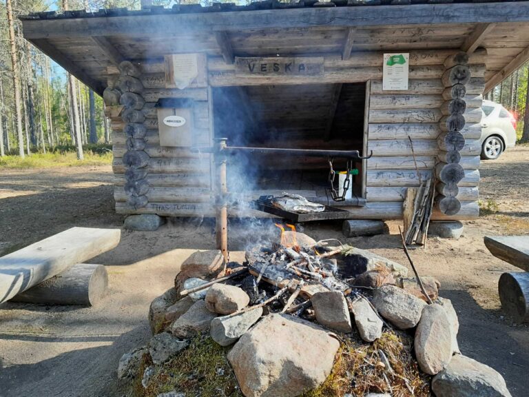 Veskan laavu, nuotiossa tulet ja talkooeväät paistumassa ritilän päällä folioon käärittynä.
