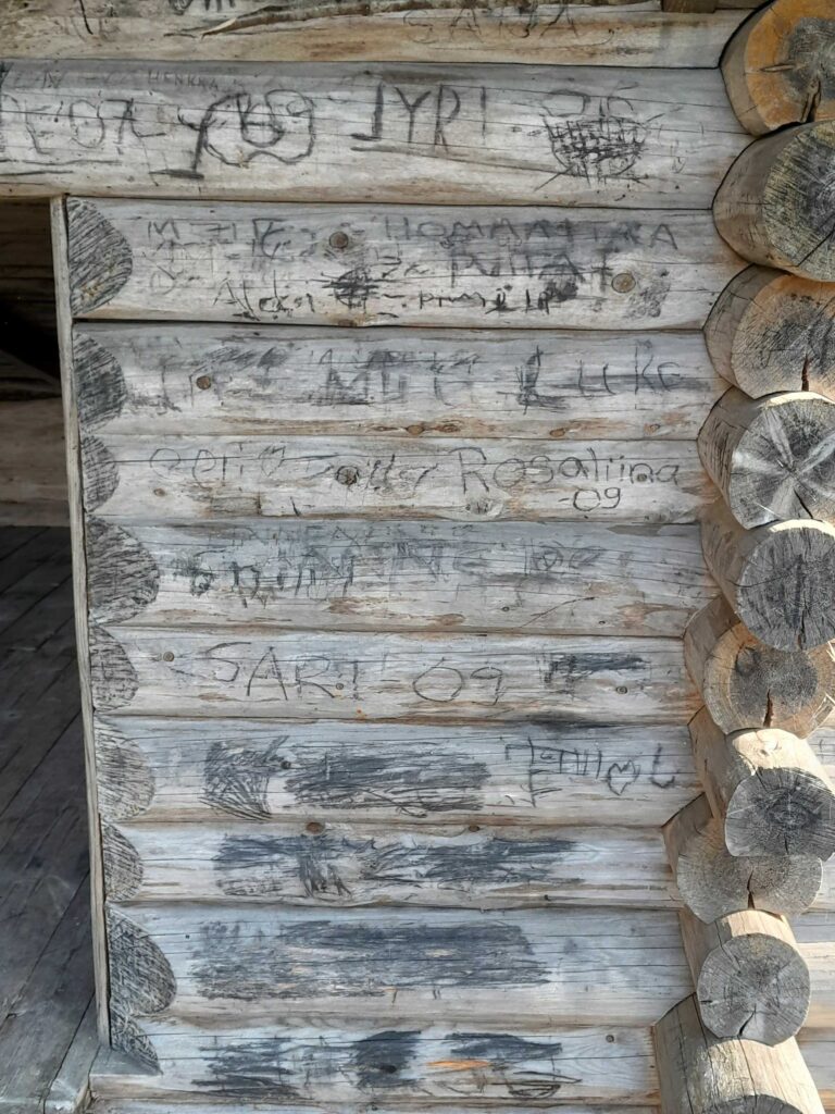 Kaiverrettuja kirjoituksia laavun seinässä.